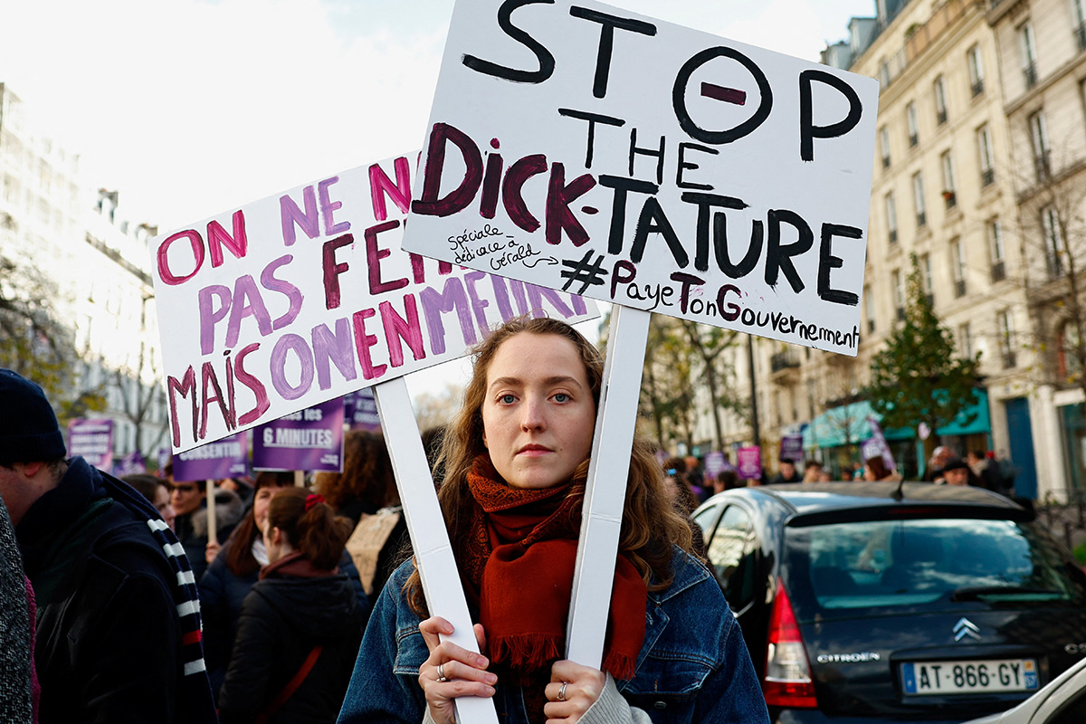 Женщина держит плакаты во время акции протеста в Париже. На том, что на переднем плане, написано: «Остановите dick-татуру». Юмор основан на схожести слова dick (грубая форма слова «пенис» в переводе с английского) и первой части французского слова dictature («диктатура»). 25 ноября 2023 года. Фото: Reuters