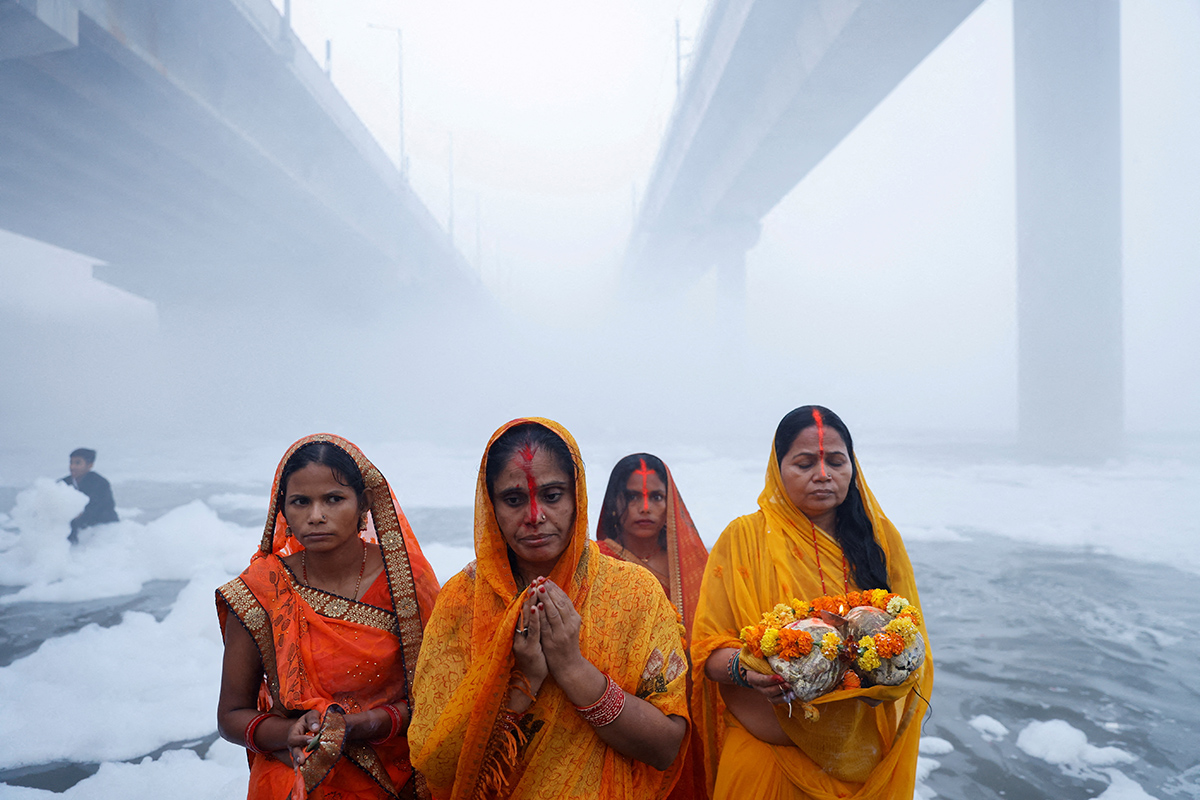 Индуистские верующие поклоняются богу Солнца, стоя среди пены, покрывающей загрязненную реку Ямуна, во время индуистского религиозного праздника Чхатх Пуджа в Нью-Дели, Индия, 20 ноября 2023 года. Фото: Reuters